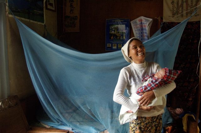 Una mamma e il suo bambino vicino al loro letto protetto dalla zanzariera come prevenzione della malaria. Foto di Valeria Turrisi.